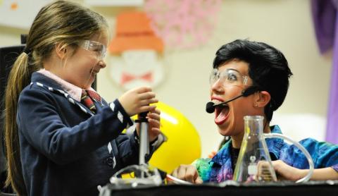 A little girl and a performer with a microphone use beakers for an experiment.